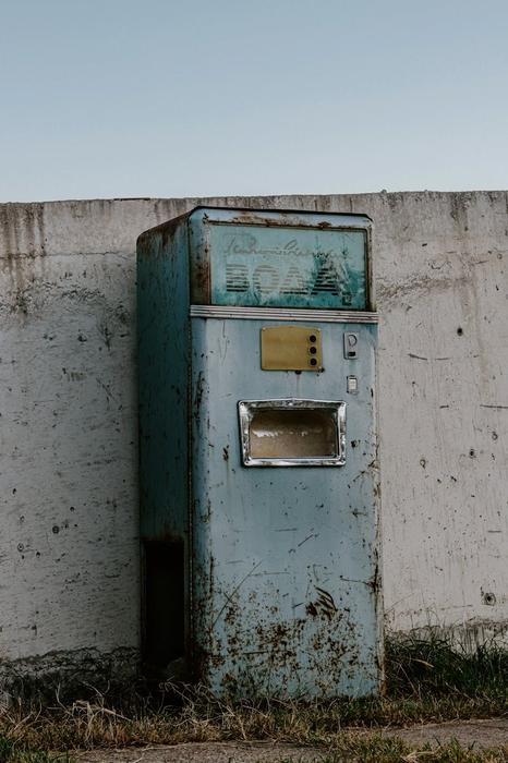 A weathered vintage soda vending machine against a concrete wall outdoors, evoking nostalgia.