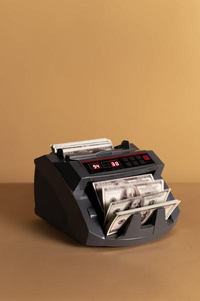 Electronic money counter processing US dollars on a neutral background.