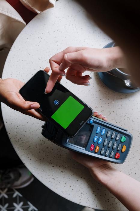 A close-up of a smartphone making a contactless payment on a terminal in a cafe setting.