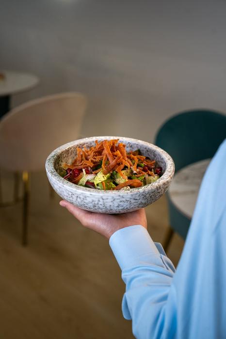 Colorful vegetable salad held by a person indoors, showcasing healthy eating in a modern dining environment.